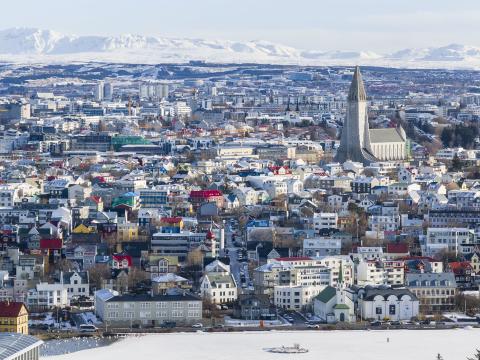 Loftmynd af Reykjavík að vetri til. Snjór, hvít fjöll í bakgrunni, Hallgrímskirkja hægra megin í rammanum fyrir miðju, Tjörnin fremst.