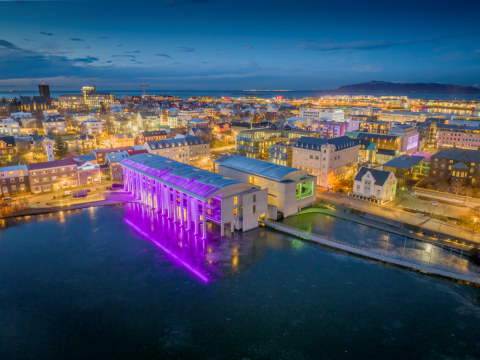 Ráðhús Reykjavíkur um vetur úr lofti lýst fjólubláum ljósum. Einnig sést Kvosin úr lofti.