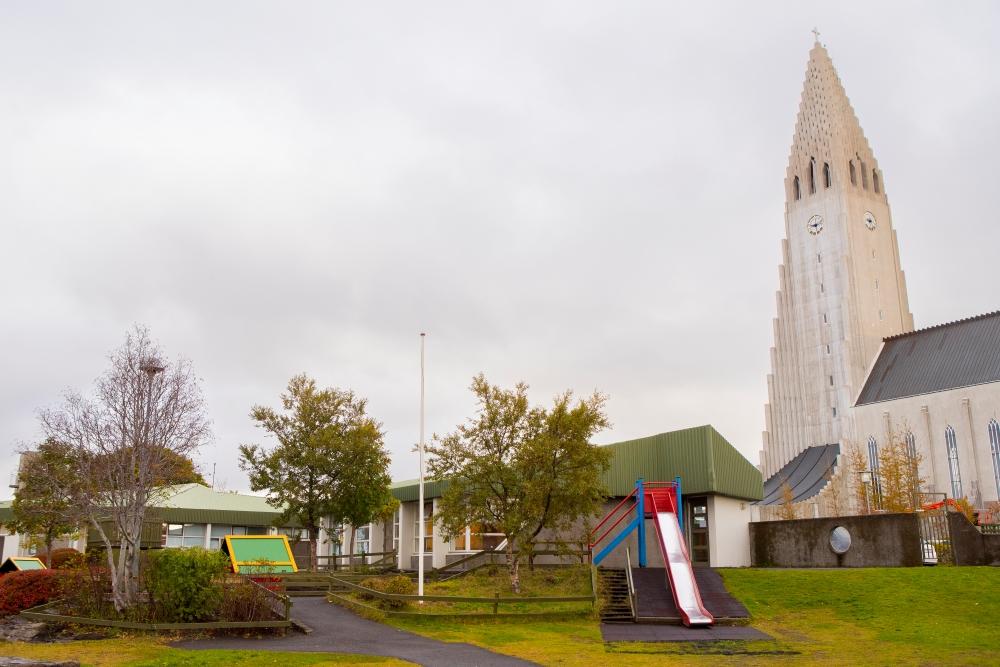 Outdoor play area at Grænaborg preschool with Hallgrímskirkja in the background. On the play area you can see a slide, tree and small house