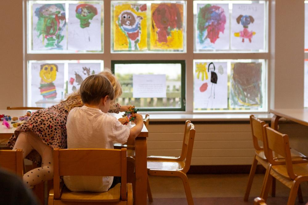 Children at Grænaborg preschool playing at a table. Artwork by the children in the window in the background.