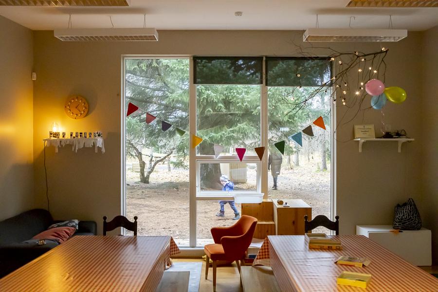 Tables and chairs at Rauðhóll Preschool in the Björnslundur building. Trees and children seen through the window
