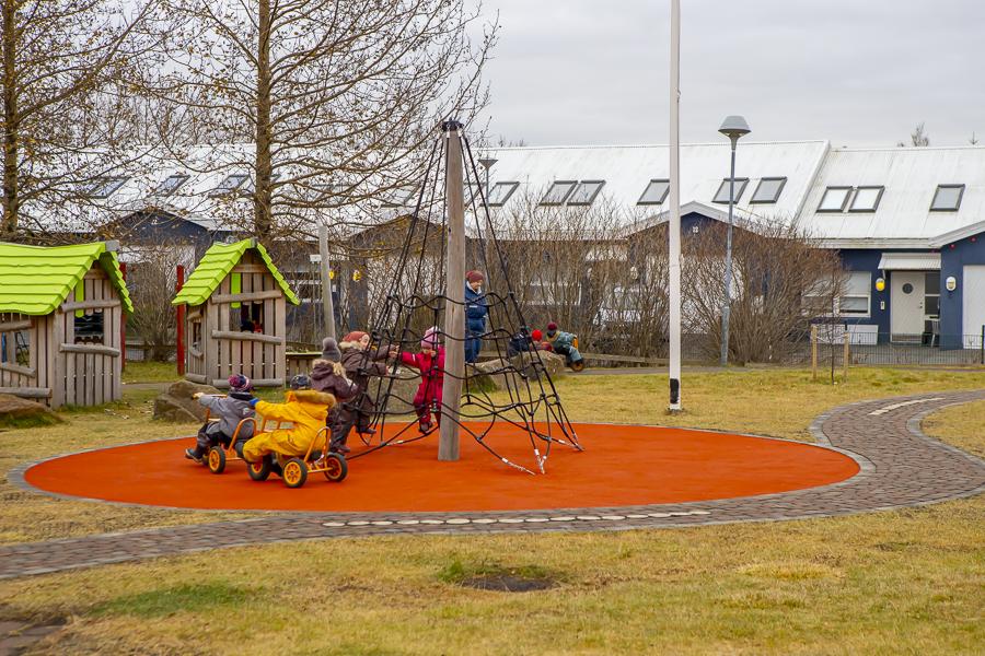 Children playing on the climbing frame and riding tricycles in Lyngheimar's outdoor play area.