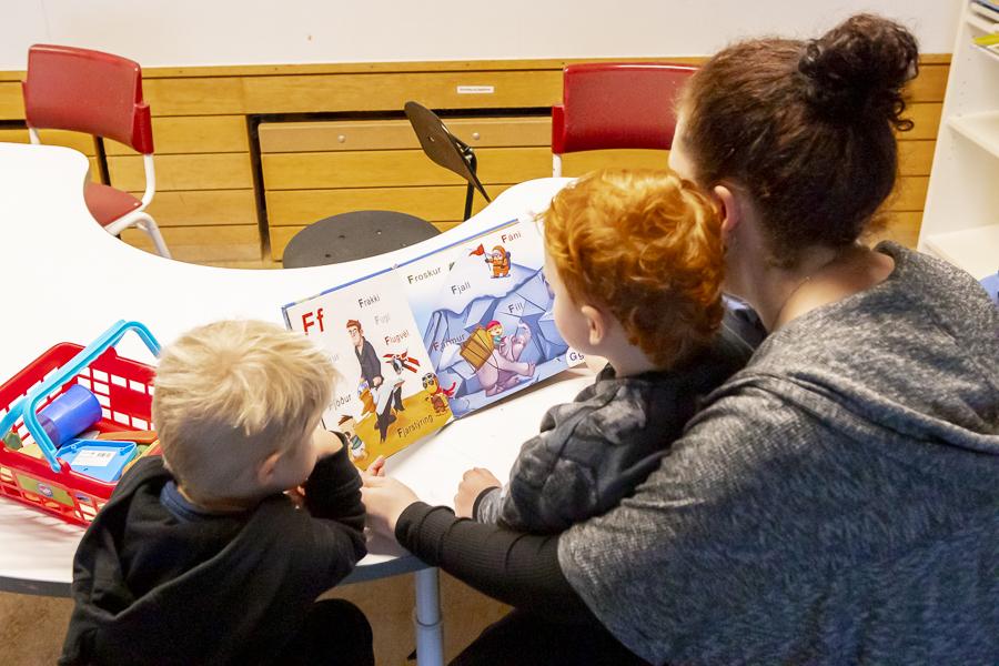 Börn sitja og skoða bók ásamt leikskólakennara