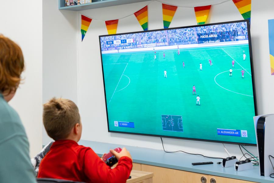 Children sit in front of a wall screen playing a soccer video game.
