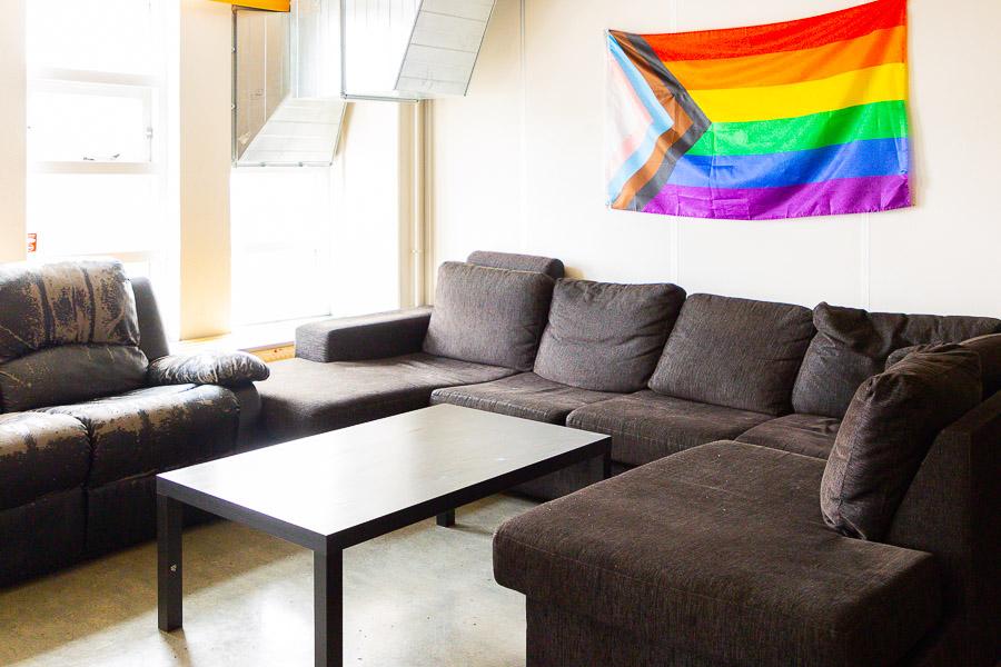 Corner couches and coffee table. Pride flag on the wall.