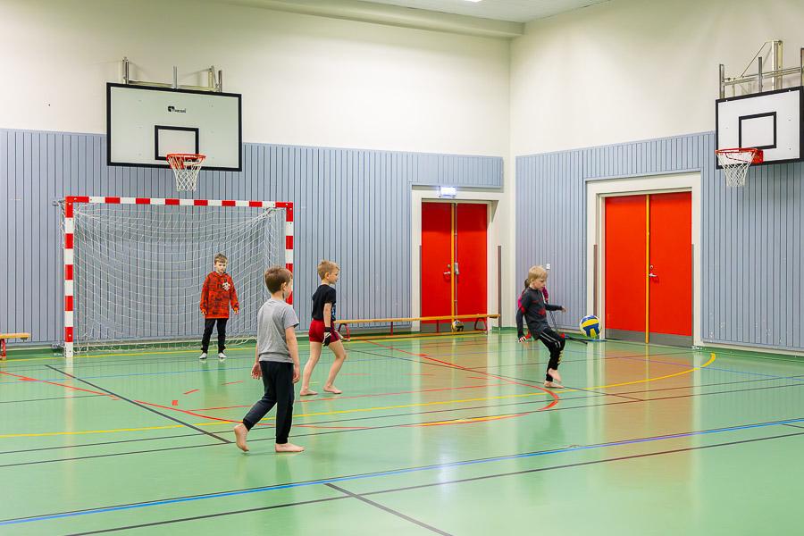 Children playing soccer on an indoor field.