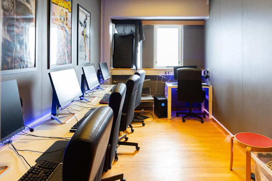 Room with a long table, computer screens and office chairs. Poster on the wall.