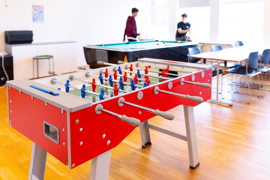 Room with a foosball table and pool table. Teenagers playing pool. 