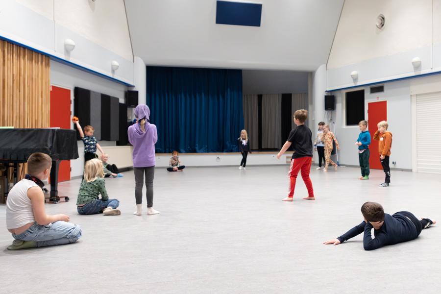 Children playing a ball game in a white hall. 