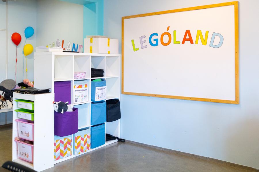 A board on the wall that reads "Lególand." A white shelf with colorful baskets and drawers. A bubble wall light in the background.