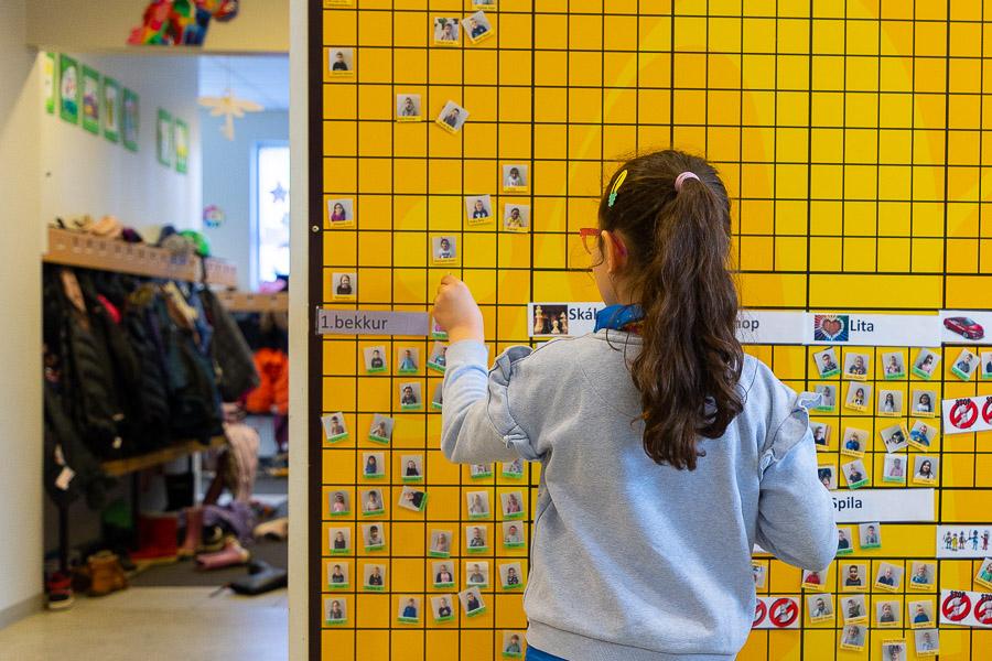 A child stands in front of a yellow wall arranging small passport photos. 