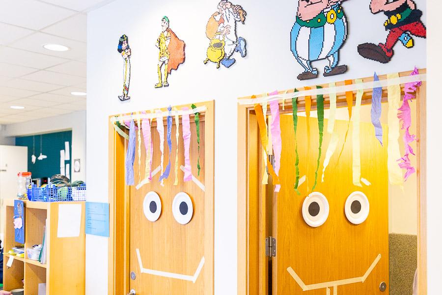 Two doors decorated with discs for eyes, tape for a mouth and tissue paper strips for hair. Figures from the Asterix and Obelix books above the doors.
