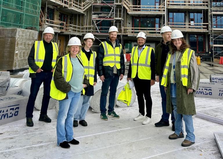 people in work clothes with hard hats and notepads with construction in the background