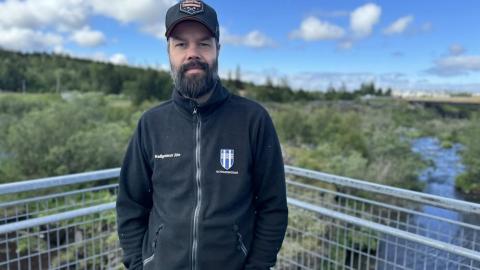 Maður á brú með skóg og á í baksýn.